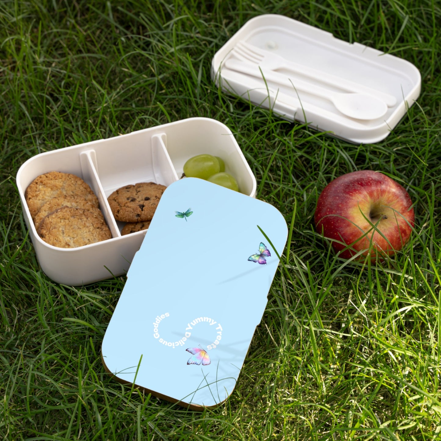 White bento box with snacks on grass next to a blue card.PBP Pub garden party food box
