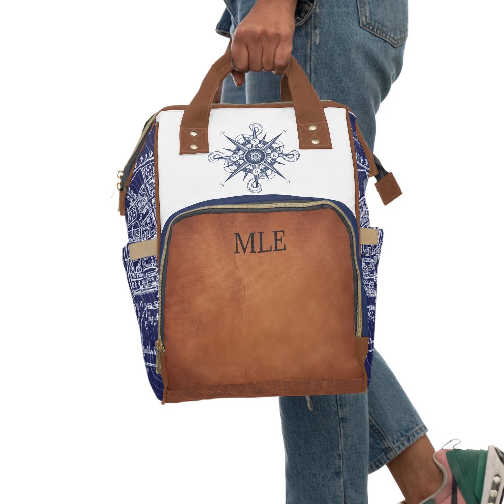 Backpack with compass design and 'MLE' initials held by a person wearing jeans.