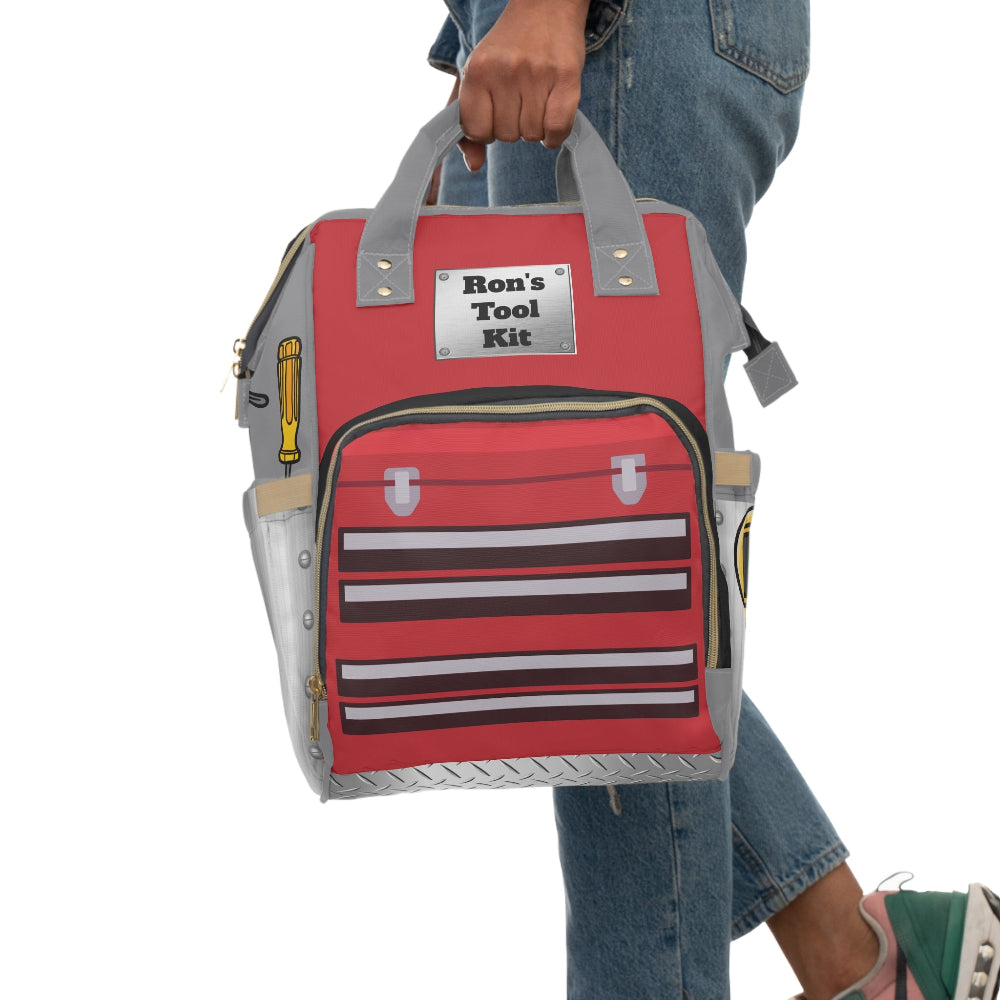 PBP Dad's Red Tool Kit Diaper Backpack with 'Ron's Tool Kit' label held by a person wearing jeans.